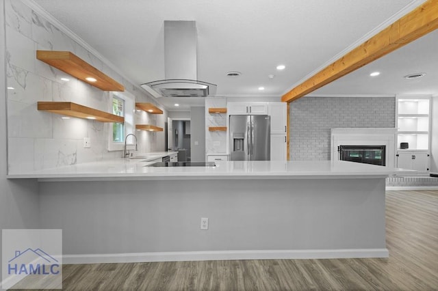 kitchen featuring stainless steel refrigerator with ice dispenser, open shelves, island exhaust hood, wood finished floors, and light countertops