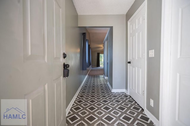 hall featuring a textured ceiling and baseboards