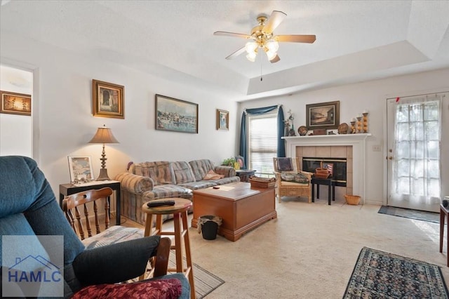 living room with light colored carpet, ceiling fan, a tray ceiling, and a tiled fireplace