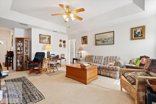 living room with ceiling fan, a raised ceiling, and light carpet