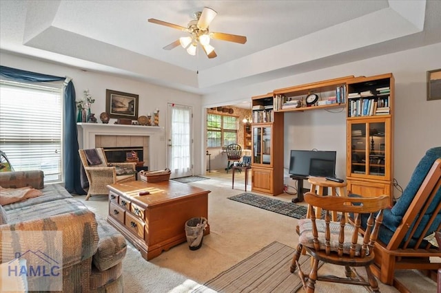 carpeted living room featuring a tile fireplace, a raised ceiling, and ceiling fan