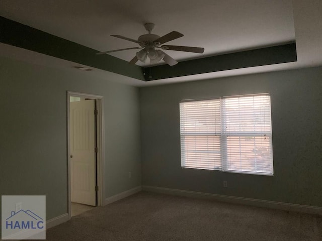 empty room featuring carpet floors, a raised ceiling, and ceiling fan