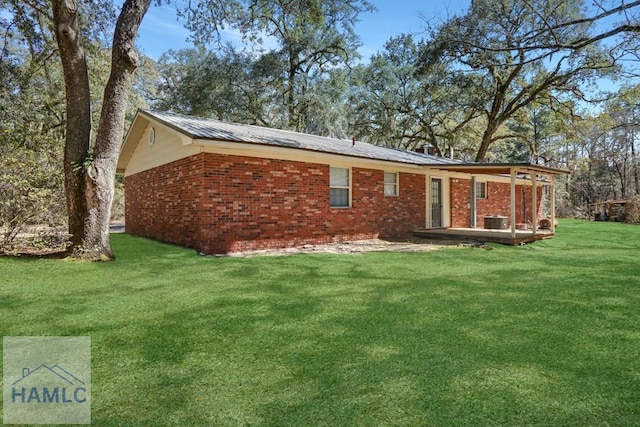 rear view of house with brick siding, central air condition unit, a wooden deck, a lawn, and metal roof