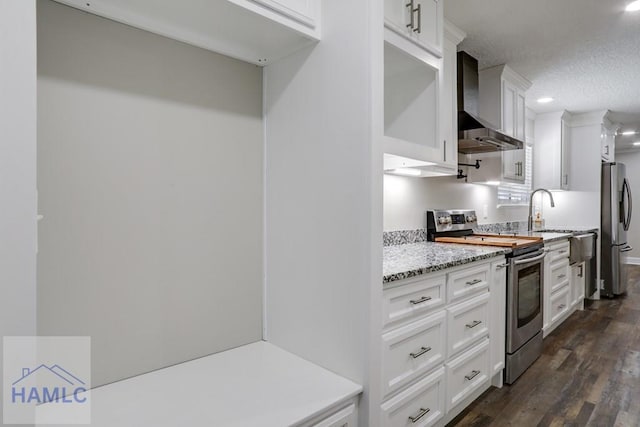 kitchen with appliances with stainless steel finishes, dark wood-style floors, white cabinets, a textured ceiling, and wall chimney exhaust hood