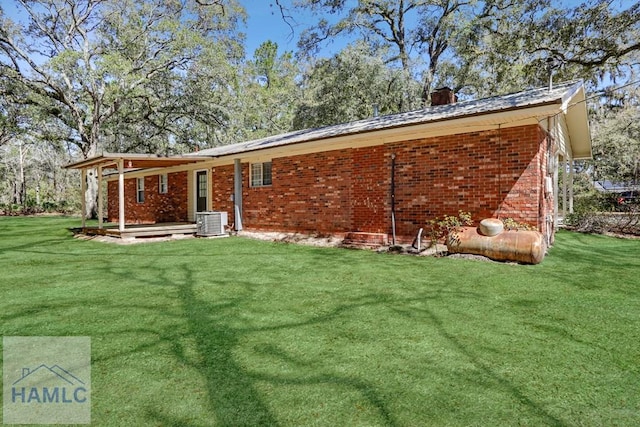 rear view of house featuring cooling unit, brick siding, a chimney, and a lawn