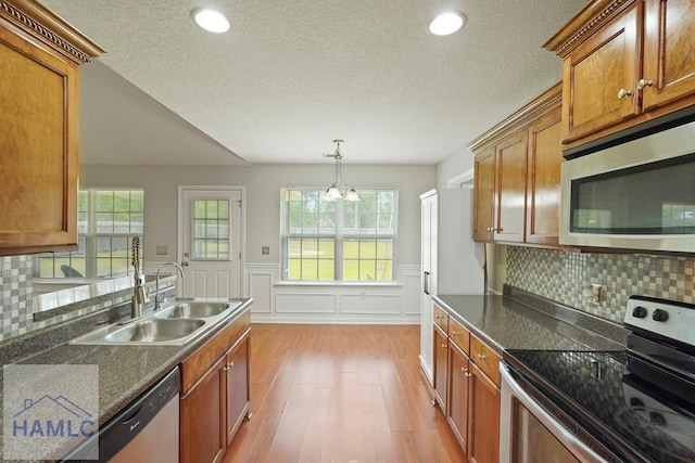 138 Forest St NE, Ludowici, GA 31316 - kitchen featuring stainless steel appliances, wood finished floors, brown cabinetry, a wainscoted wall, and a textured ceiling