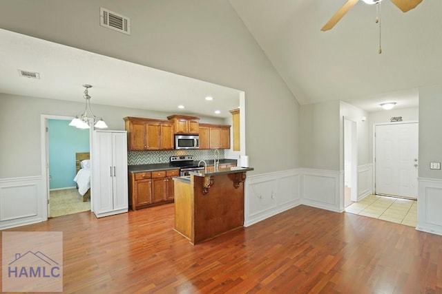 138 Forest St NE, Ludowici, GA 31316 - kitchen featuring stainless steel appliances, brown cabinetry, dark countertops, a wainscoted wall, and wood finished floors