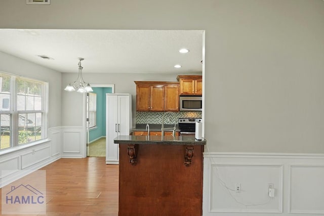 138 Forest St NE, Ludowici, GA 31316 - kitchen featuring stainless steel appliances, a chandelier, wood finished floors, brown cabinets, and a wainscoted wall
