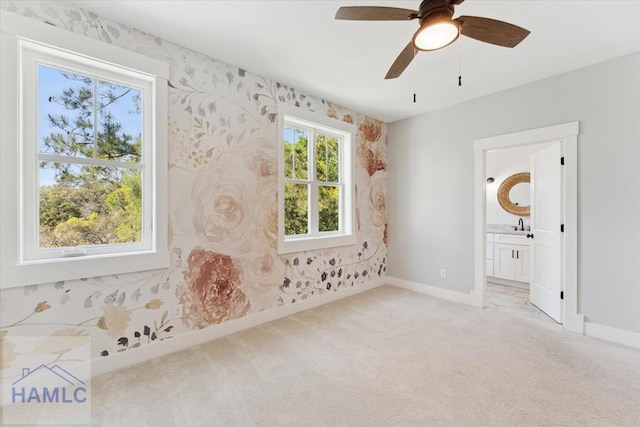 interior space with connected bathroom, light colored carpet, wallpapered walls, ceiling fan, and baseboards