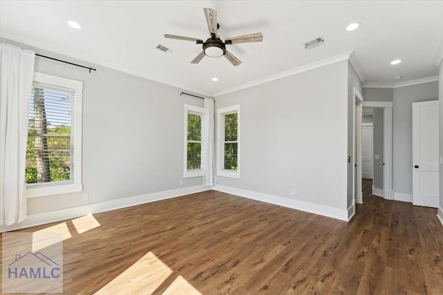 empty room featuring wood finished floors, visible vents, a healthy amount of sunlight, and crown molding