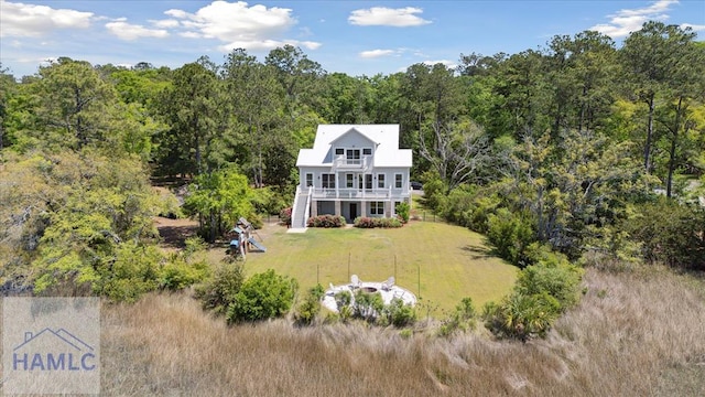 rear view of house featuring stairway, a balcony, a view of trees, and a lawn
