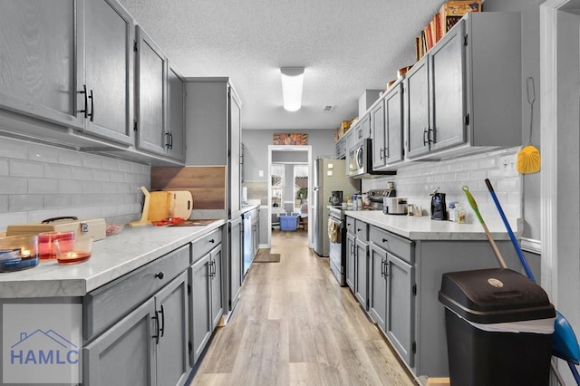 kitchen featuring appliances with stainless steel finishes, backsplash, light hardwood / wood-style flooring, and gray cabinetry