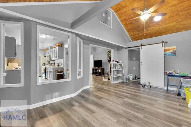 interior space featuring light wood-type flooring, ceiling fan, beam ceiling, a barn door, and high vaulted ceiling