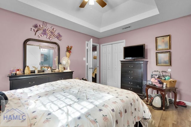 bedroom with a raised ceiling, ceiling fan, a closet, and hardwood / wood-style flooring