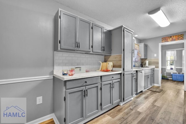 kitchen with stainless steel dishwasher, light hardwood / wood-style floors, gray cabinetry, and backsplash