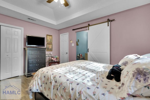 bedroom with ceiling fan, a barn door, and light wood-type flooring