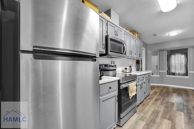 kitchen with gray cabinetry, stainless steel appliances, backsplash, light hardwood / wood-style floors, and a textured ceiling