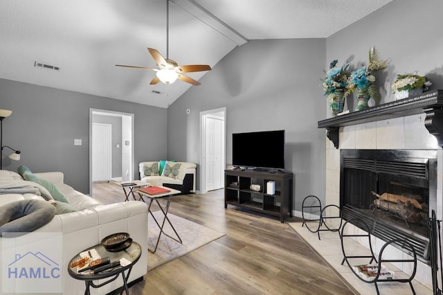 living room with a tile fireplace, ceiling fan, wood-type flooring, and vaulted ceiling