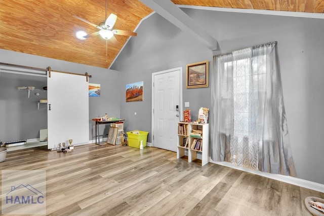 interior space with ceiling fan, a barn door, light hardwood / wood-style floors, and high vaulted ceiling