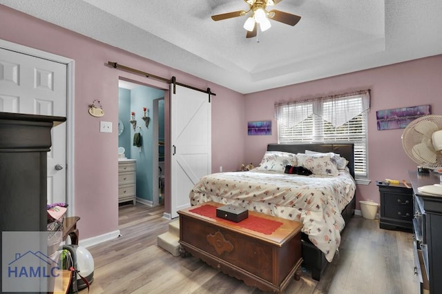 bedroom with ceiling fan, a barn door, wood-type flooring, and a textured ceiling