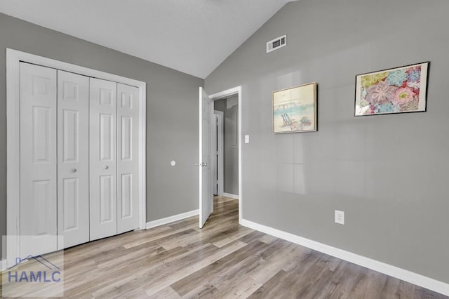 unfurnished bedroom with a closet, light hardwood / wood-style flooring, and lofted ceiling