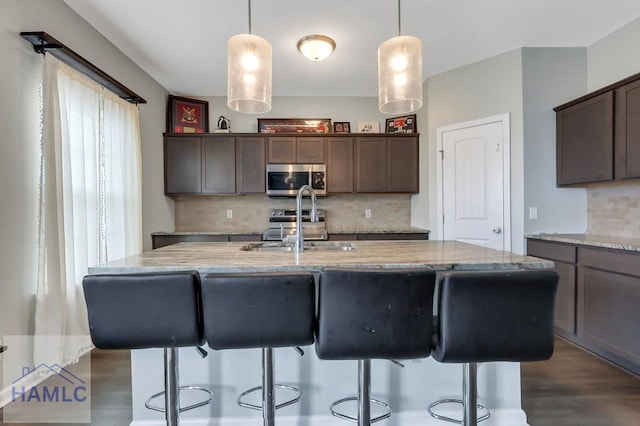 kitchen featuring a center island with sink, dark wood-style flooring, a kitchen bar, backsplash, and appliances with stainless steel finishes