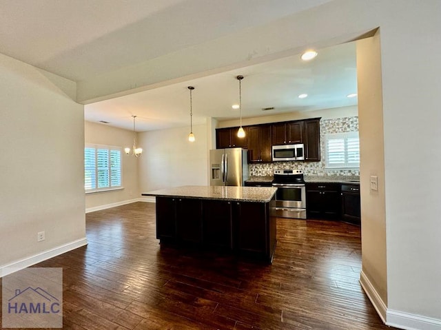 kitchen with a kitchen island, appliances with stainless steel finishes, hanging light fixtures, dark brown cabinetry, and light stone counters