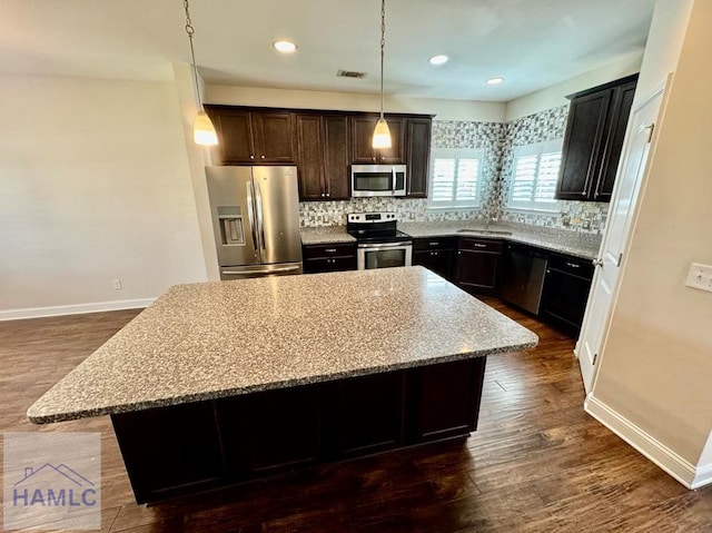 kitchen with light stone counters, appliances with stainless steel finishes, a center island, and hanging light fixtures