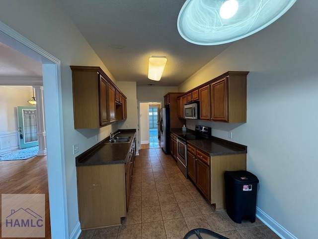 kitchen featuring dark countertops, appliances with stainless steel finishes, a sink, baseboards, and light tile patterned floors