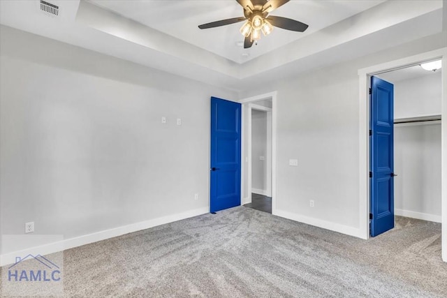unfurnished bedroom with carpet, baseboards, a walk in closet, a tray ceiling, and a closet