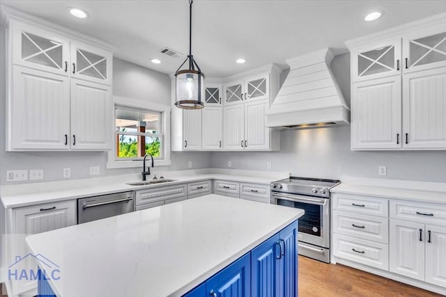 kitchen featuring custom range hood, stainless steel appliances, a sink, blue cabinets, and white cabinetry