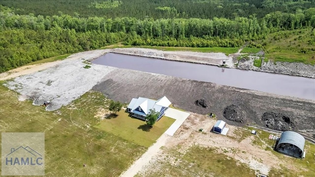 aerial view of property and surrounding area featuring a forest and a nearby body of water