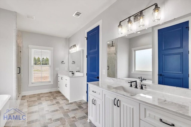full bathroom with a shower stall, baseboards, two vanities, a freestanding bath, and stone finish floors
