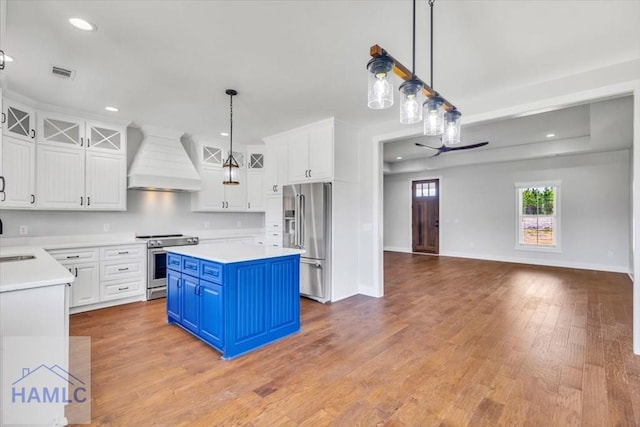 kitchen featuring stainless steel appliances, custom range hood, blue cabinets, white cabinetry, and recessed lighting