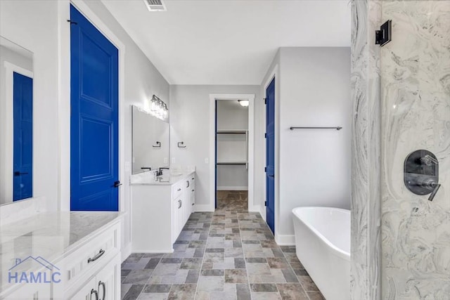 bathroom with a soaking tub, vanity, baseboards, a spacious closet, and stone finish floors
