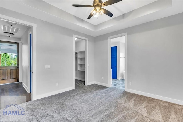 unfurnished bedroom with baseboards, a raised ceiling, carpet floors, a spacious closet, and ensuite bath