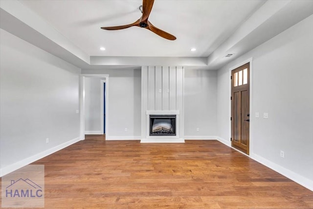 unfurnished living room with a ceiling fan, a raised ceiling, a fireplace, wood finished floors, and recessed lighting