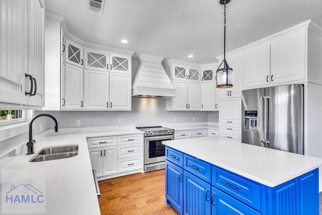 kitchen featuring stainless steel appliances, blue cabinets, premium range hood, a sink, and white cabinets