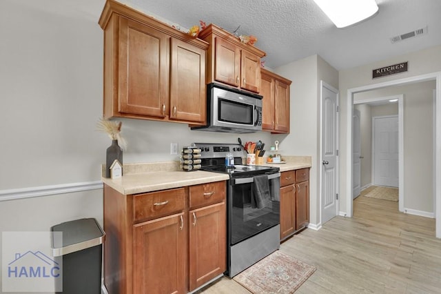 kitchen featuring stainless steel appliances, a textured ceiling, and light hardwood / wood-style floors