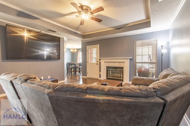 living room with hardwood / wood-style floors, plenty of natural light, a tray ceiling, a textured ceiling, and a tiled fireplace