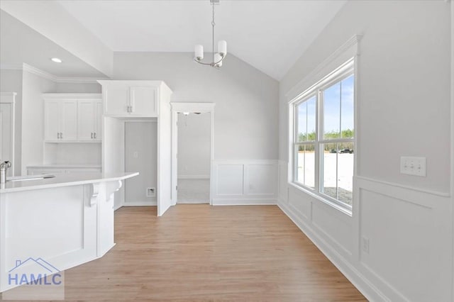 unfurnished dining area featuring lofted ceiling, light wood-style flooring, a sink, a decorative wall, and a notable chandelier