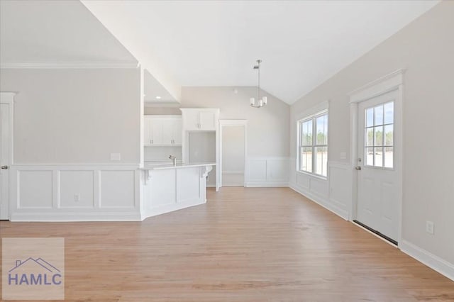 unfurnished living room with vaulted ceiling, crown molding, a notable chandelier, and light wood-style floors