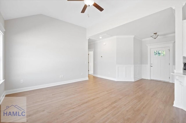 spare room featuring lofted ceiling, ornamental molding, wainscoting, light wood-style floors, and a ceiling fan