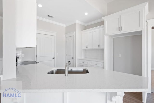 kitchen with light stone countertops, a peninsula, a sink, white cabinets, and crown molding