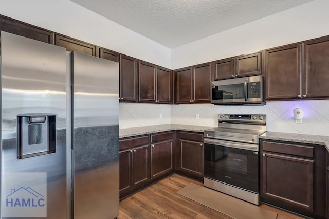 kitchen featuring dark wood finished floors, dark brown cabinetry, backsplash, and stainless steel appliances