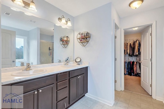 bathroom with a walk in closet, double vanity, visible vents, and a sink