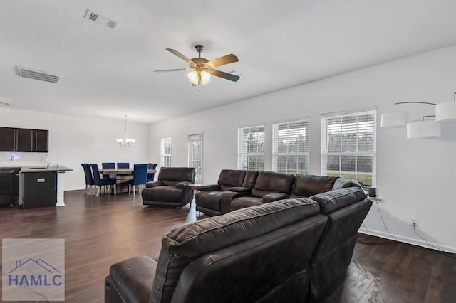 living area with visible vents, baseboards, dark wood-style floors, and ceiling fan with notable chandelier