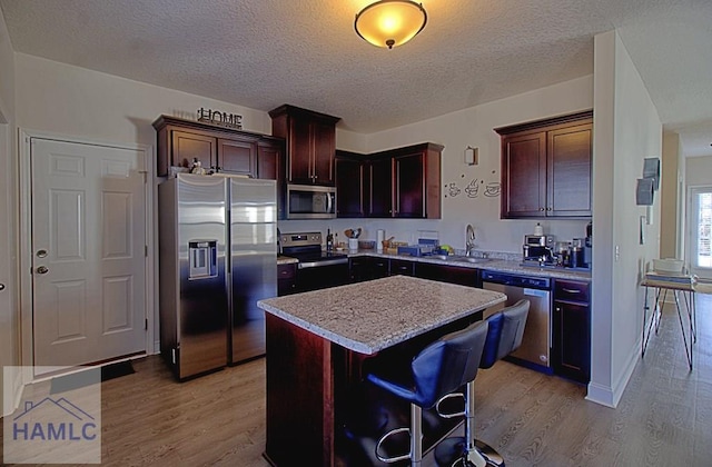 kitchen featuring a center island, sink, a textured ceiling, appliances with stainless steel finishes, and a kitchen bar