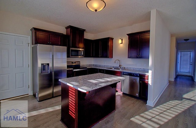 kitchen featuring sink, light stone counters, a center island, appliances with stainless steel finishes, and light hardwood / wood-style floors