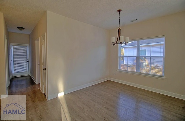 empty room featuring an inviting chandelier, dark hardwood / wood-style floors, and a textured ceiling